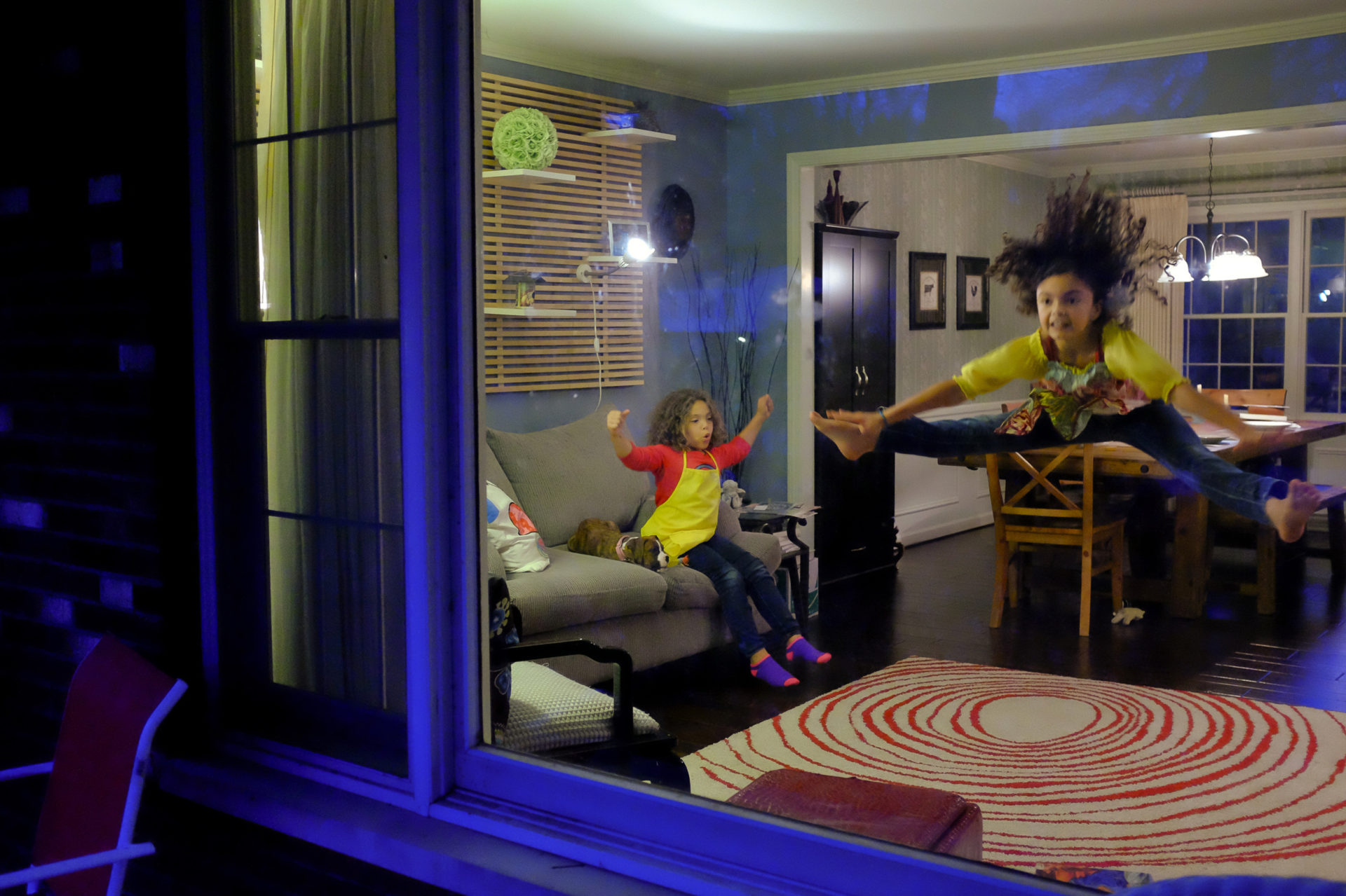 Two young girls can be seen playing in a home through a front window